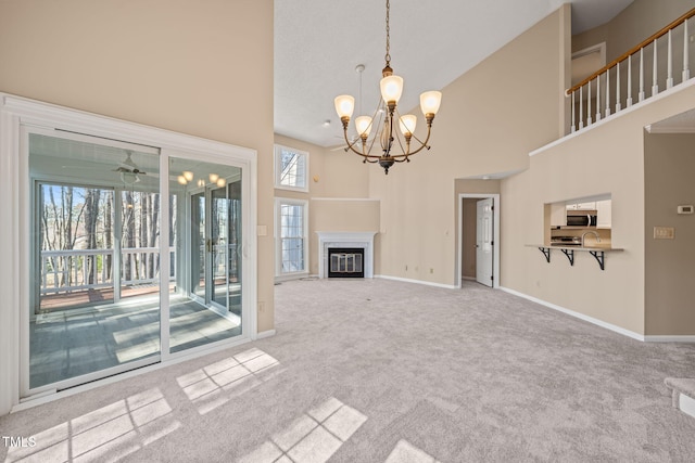 unfurnished living room featuring baseboards, a fireplace with flush hearth, a towering ceiling, carpet flooring, and ceiling fan with notable chandelier