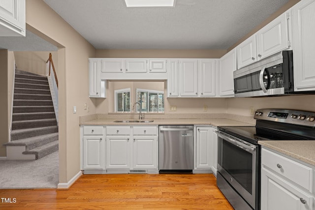 kitchen featuring light countertops, light wood-style floors, white cabinets, stainless steel appliances, and a sink