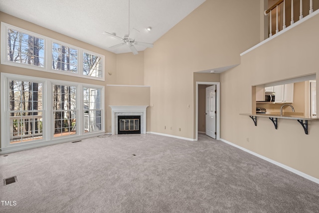 unfurnished living room featuring visible vents, light carpet, baseboards, and ceiling fan