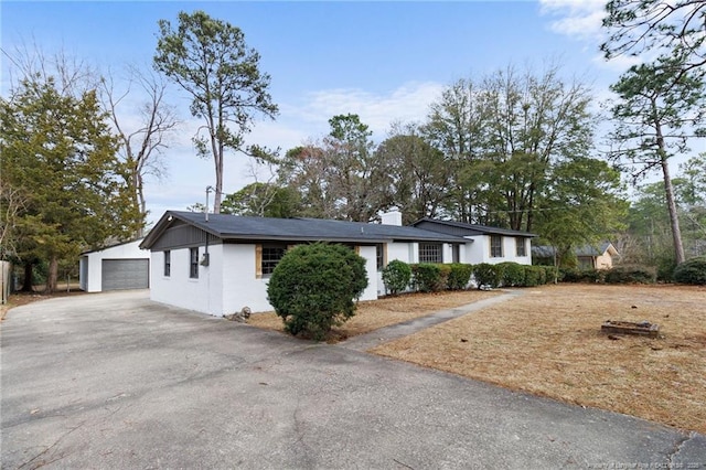 single story home featuring a garage, a chimney, and an outbuilding