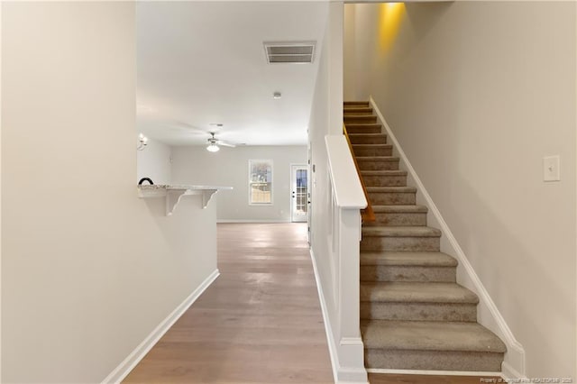 stairway featuring baseboards, visible vents, ceiling fan, and wood finished floors