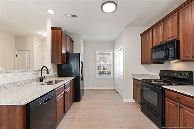 kitchen featuring visible vents, light wood-style floors, light stone countertops, black appliances, and a sink