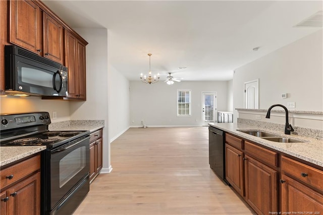 kitchen with light wood-style floors, open floor plan, light stone countertops, black appliances, and a sink