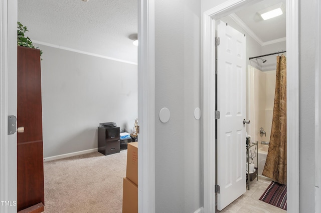 hallway with light carpet, baseboards, ornamental molding, and a textured ceiling