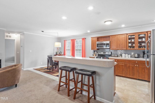 kitchen featuring stainless steel appliances, light countertops, backsplash, brown cabinets, and a kitchen bar