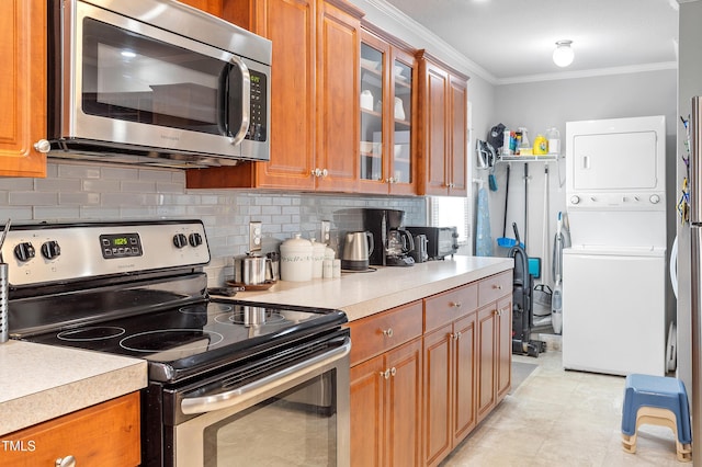 kitchen featuring appliances with stainless steel finishes, stacked washer / drying machine, brown cabinetry, and crown molding