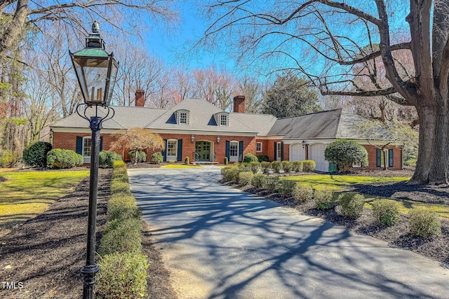 view of front of house featuring an attached garage, brick siding, driveway, and a chimney