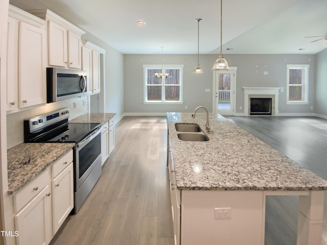 kitchen with stainless steel appliances, decorative backsplash, white cabinetry, a sink, and an island with sink