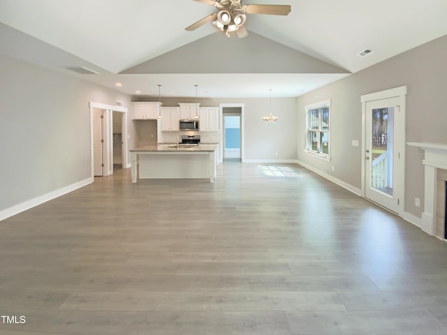 unfurnished living room with lofted ceiling, light wood-style flooring, a glass covered fireplace, baseboards, and ceiling fan with notable chandelier