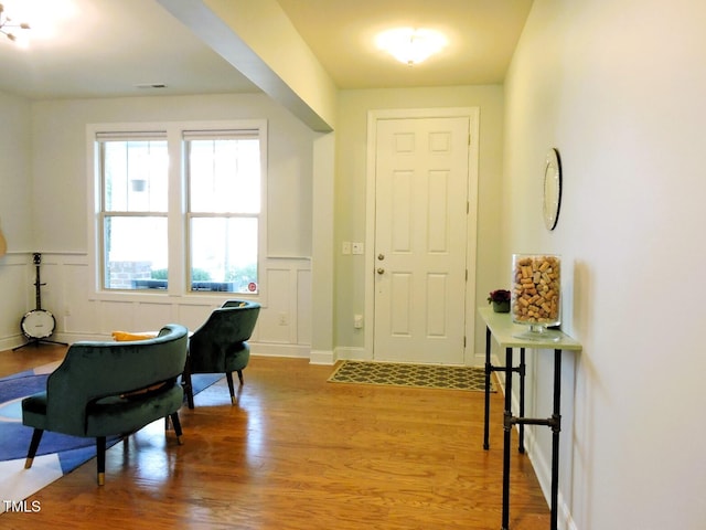 foyer with a wainscoted wall, a decorative wall, visible vents, and wood finished floors