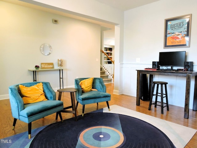 sitting room with wood finished floors, wainscoting, a decorative wall, and stairs