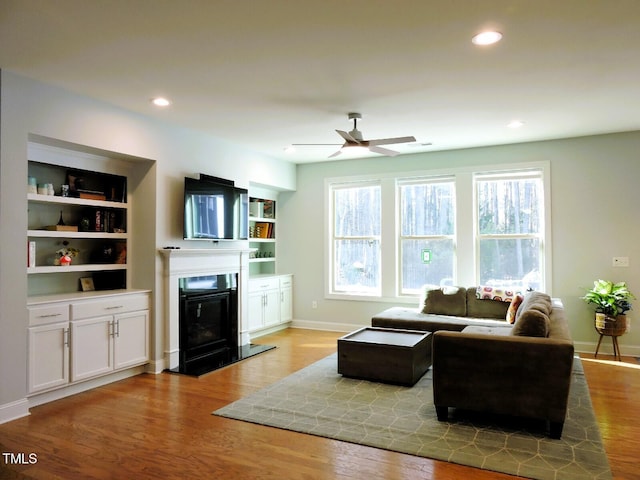 living area with a glass covered fireplace, baseboards, recessed lighting, and wood finished floors