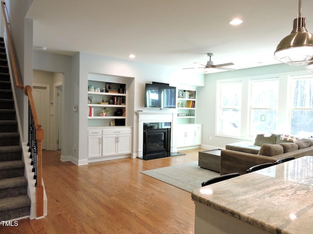 unfurnished living room featuring recessed lighting, light wood-style flooring, stairway, a ceiling fan, and a glass covered fireplace