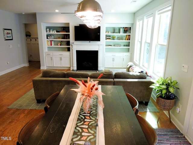 living room featuring built in shelves, recessed lighting, a fireplace, wood finished floors, and baseboards