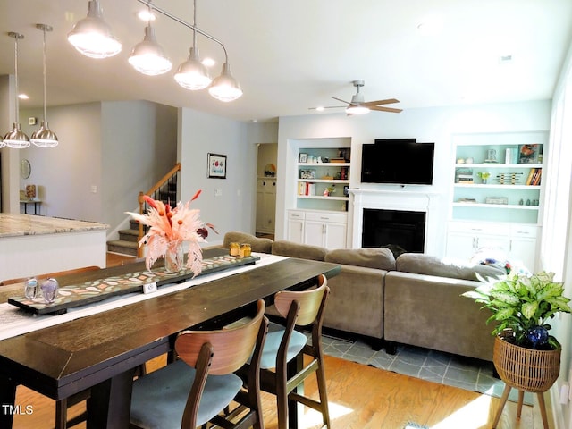 dining area with a ceiling fan, light wood-style flooring, stairway, built in shelves, and a fireplace