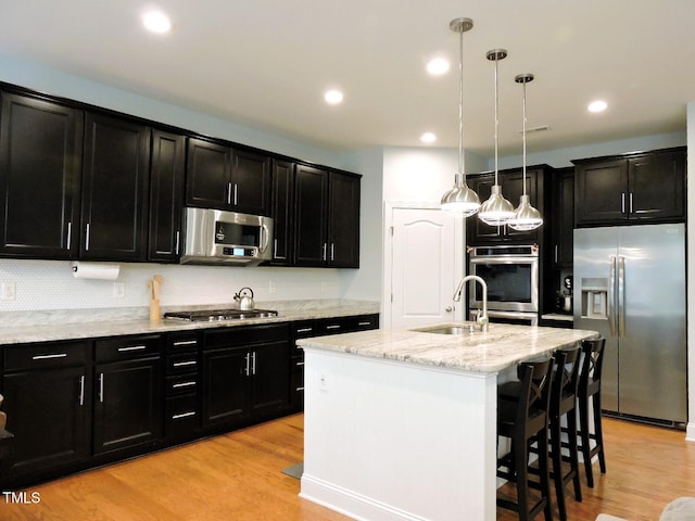 kitchen featuring appliances with stainless steel finishes, a sink, light wood-style flooring, and dark cabinets