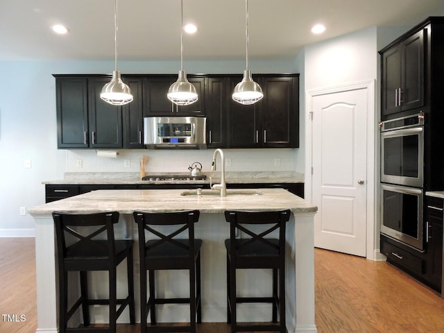 kitchen with light stone counters, a breakfast bar area, stainless steel appliances, a sink, and light wood-type flooring