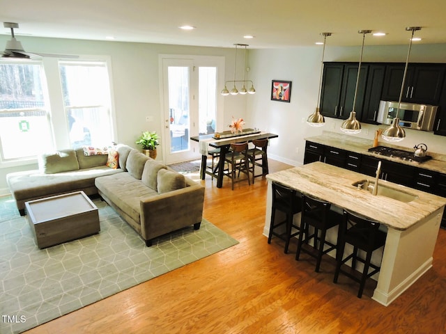 kitchen with a breakfast bar, appliances with stainless steel finishes, light wood-style floors, a sink, and dark cabinets