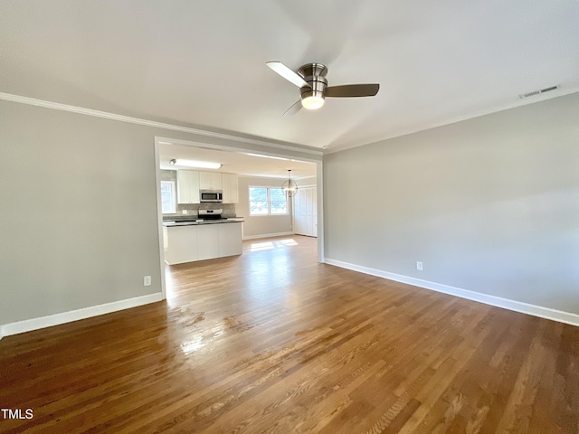 unfurnished living room featuring ornamental molding, ceiling fan with notable chandelier, baseboards, and wood finished floors