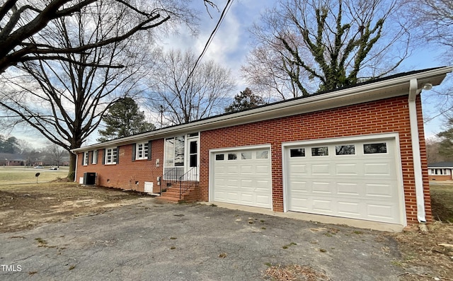 exterior space with driveway, central AC unit, crawl space, an attached garage, and brick siding