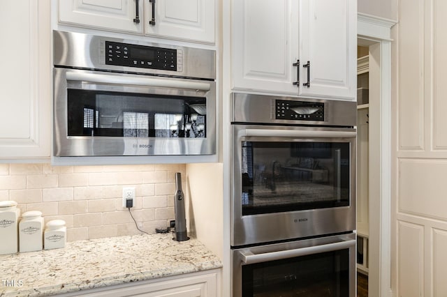 kitchen with backsplash, light stone countertops, double oven, and white cabinets