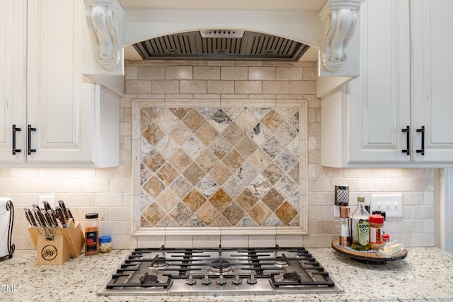 kitchen with stainless steel gas cooktop, arched walkways, custom range hood, white cabinetry, and tasteful backsplash