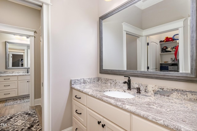 full bathroom featuring vanity, a walk in closet, baseboards, and wood finished floors