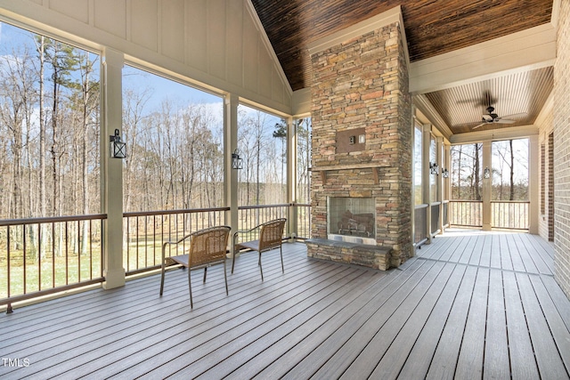 unfurnished sunroom featuring wood ceiling, an outdoor stone fireplace, a ceiling fan, and vaulted ceiling