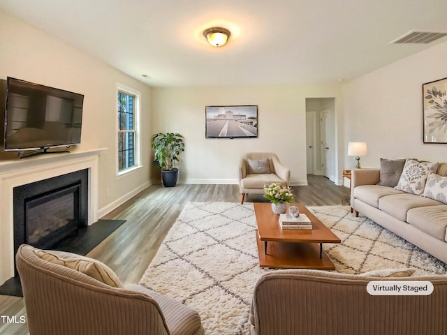 living room with a glass covered fireplace, visible vents, baseboards, and wood finished floors