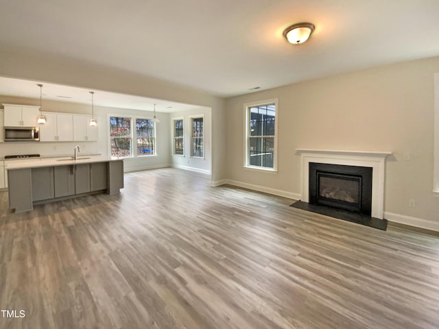 unfurnished living room featuring a fireplace with flush hearth, baseboards, a sink, and wood finished floors