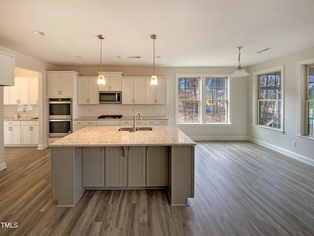 kitchen with stainless steel appliances, wood finished floors, a sink, and white cabinetry