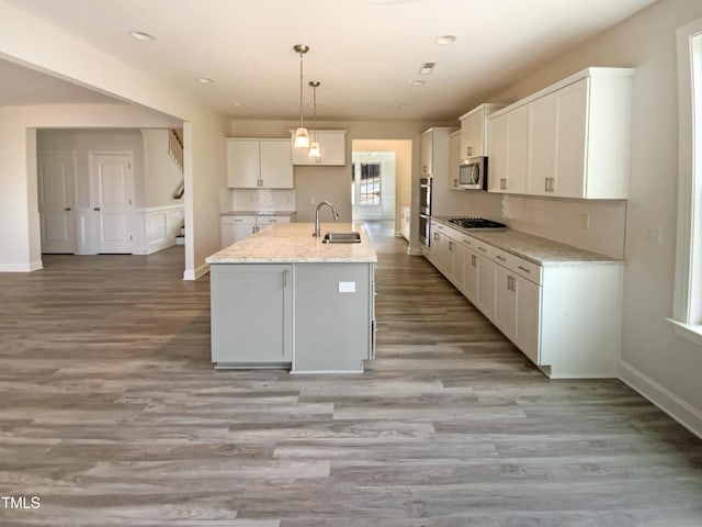 kitchen with white cabinets, stainless steel microwave, decorative light fixtures, light stone countertops, and a sink