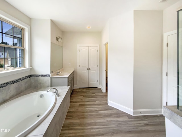 full bathroom featuring wood finished floors, a garden tub, vanity, and baseboards