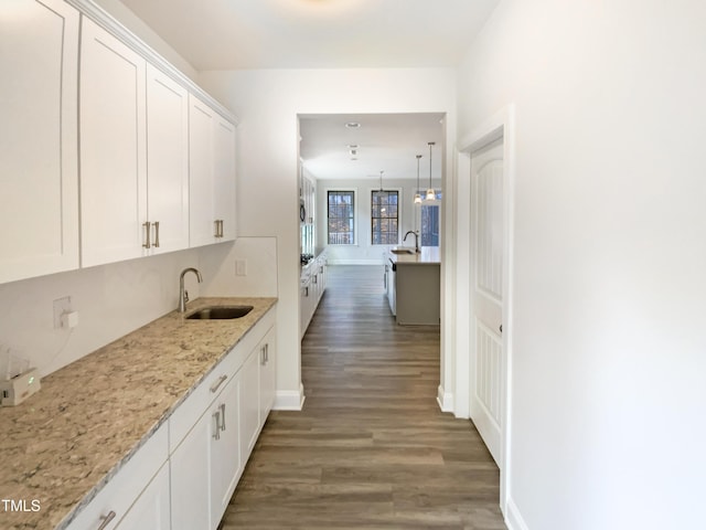 kitchen with wood finished floors, a sink, light stone counters, and white cabinets