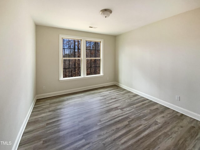 spare room with dark wood-style flooring, visible vents, and baseboards