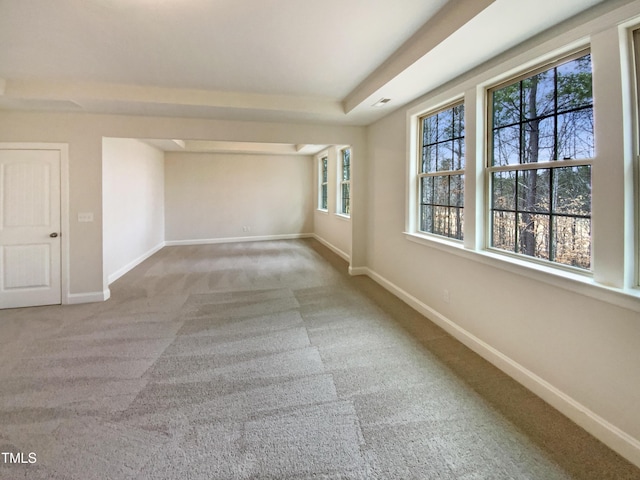 empty room with carpet floors, a tray ceiling, and baseboards