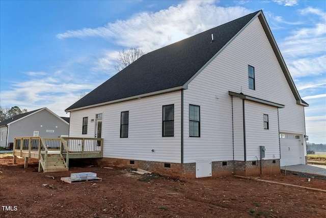 rear view of property featuring an attached garage, driveway, roof with shingles, crawl space, and a wooden deck