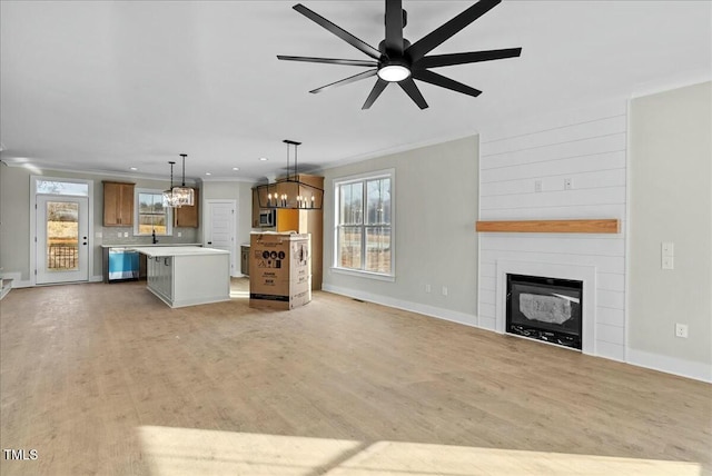 unfurnished living room with light wood-style flooring, ceiling fan with notable chandelier, a fireplace, baseboards, and ornamental molding