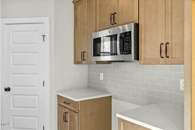 kitchen featuring brown cabinets, light countertops, stainless steel microwave, and decorative backsplash