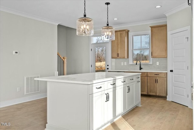 kitchen featuring crown molding, light wood finished floors, visible vents, backsplash, and a sink