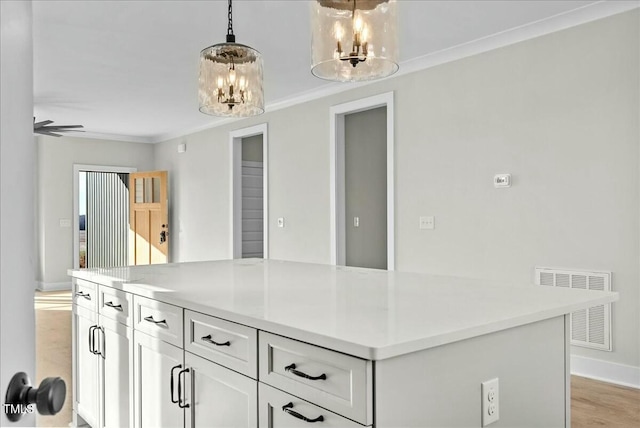 kitchen with visible vents, ornamental molding, white cabinetry, a kitchen island, and a chandelier