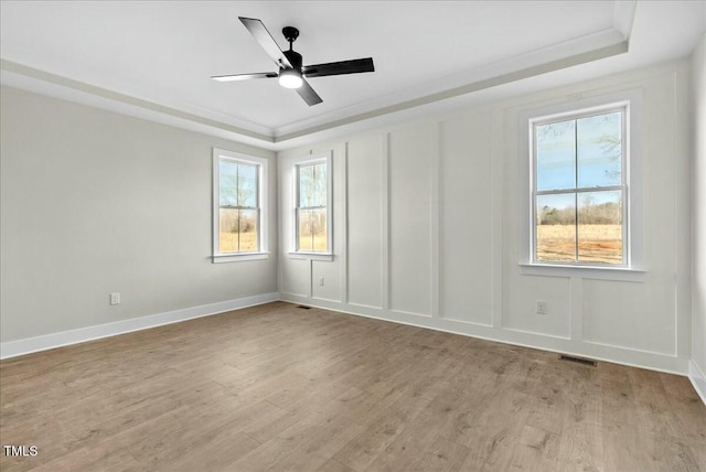 empty room featuring a raised ceiling, light wood-style flooring, and a decorative wall