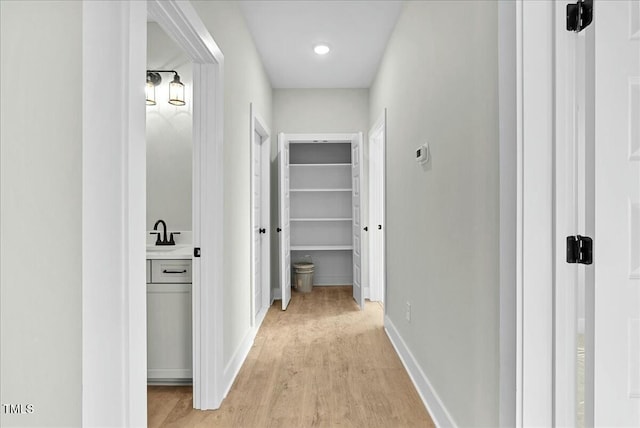 corridor with baseboards, a sink, and light wood-style floors