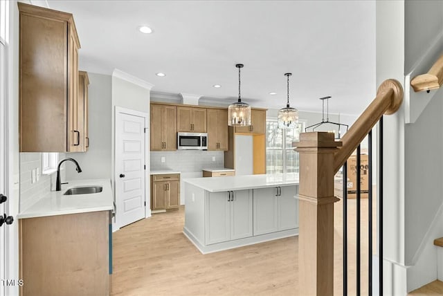 kitchen with decorative backsplash, stainless steel microwave, ornamental molding, light wood-style floors, and a sink