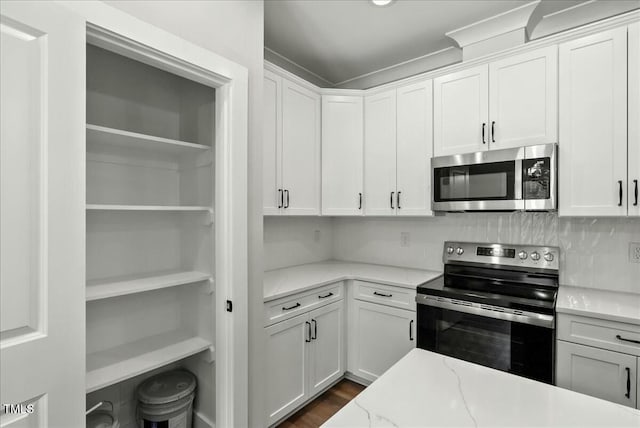 kitchen featuring stainless steel appliances, light stone countertops, white cabinets, and tasteful backsplash