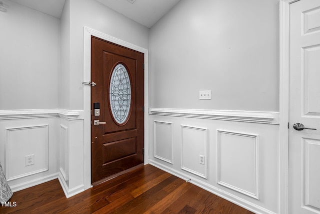 foyer featuring dark wood-style floors, a decorative wall, and wainscoting