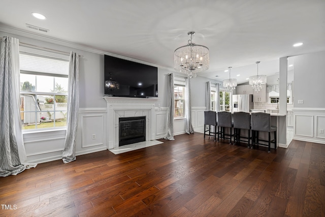 living room featuring visible vents, dark wood-style floors, a fireplace, a chandelier, and a decorative wall