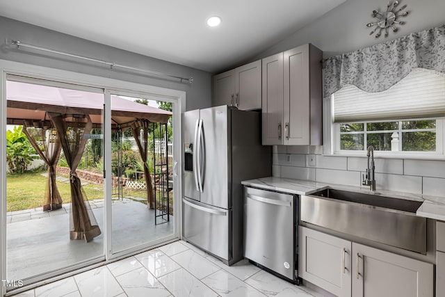 kitchen with a sink, marble finish floor, appliances with stainless steel finishes, backsplash, and light stone countertops