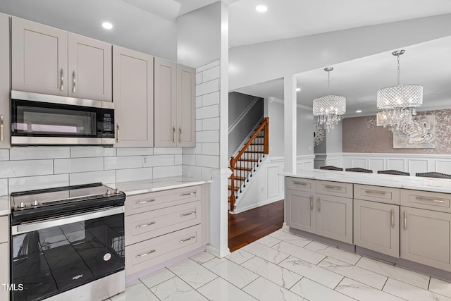 kitchen featuring marble finish floor, a wainscoted wall, pendant lighting, gray cabinetry, and appliances with stainless steel finishes