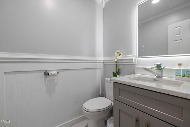 half bathroom featuring ornamental molding, a wainscoted wall, vanity, and toilet